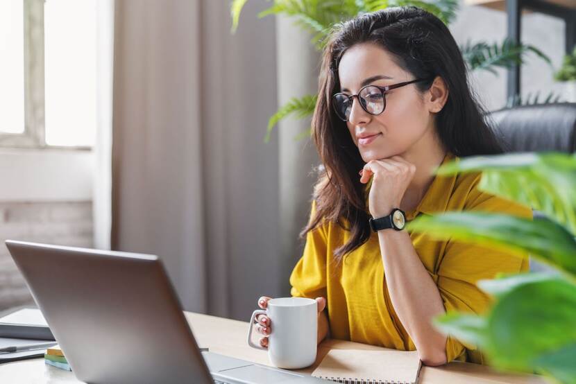 Jonge vrouw zittend achter laptop met kopje in haar hand